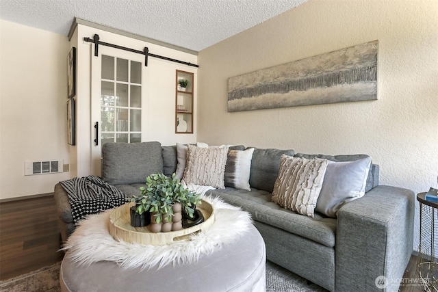 living area featuring visible vents, a barn door, a textured ceiling, and wood finished floors