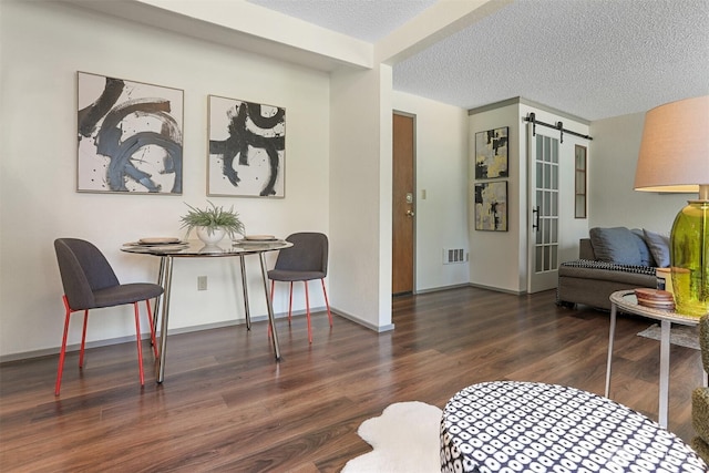 living area with a textured ceiling, visible vents, wood finished floors, a barn door, and baseboards