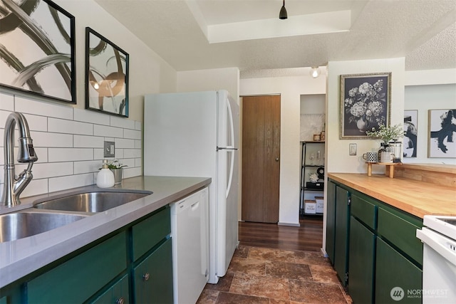 kitchen featuring stone finish floor, decorative backsplash, a sink, green cabinetry, and white appliances