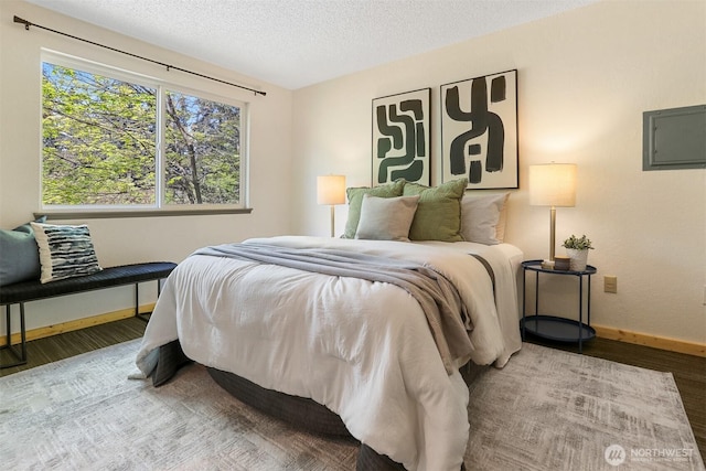 bedroom featuring a textured ceiling, baseboards, wood finished floors, and electric panel
