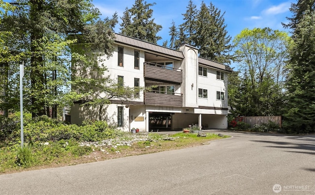 view of front facade with aphalt driveway, fence, a balcony, stucco siding, and a carport
