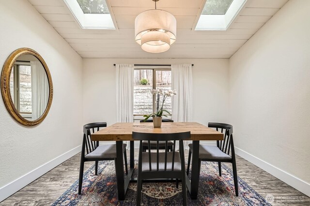 dining area with dark wood-style flooring, a skylight, wooden ceiling, and baseboards