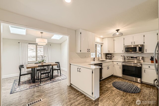 kitchen with a sink, stainless steel appliances, dark wood-type flooring, a skylight, and visible vents