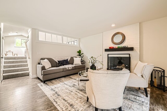 living room featuring a brick fireplace, baseboards, wood finished floors, lofted ceiling, and stairway
