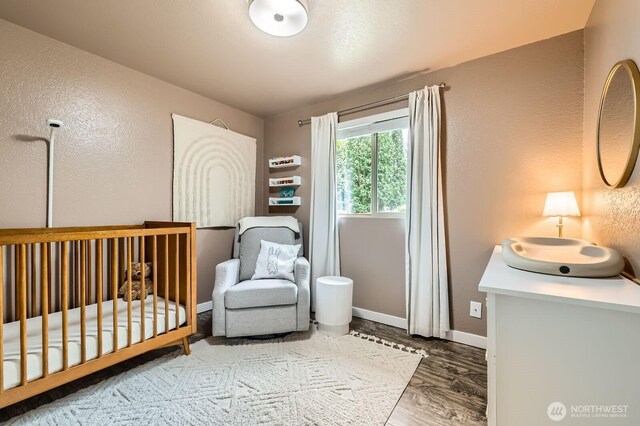 bedroom featuring a nursery area, baseboards, a textured wall, and wood finished floors