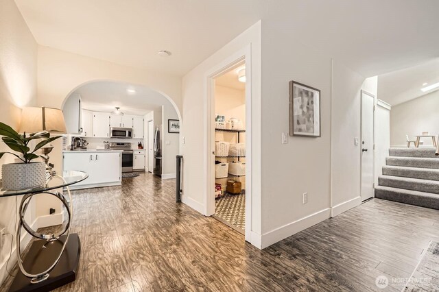 hall featuring stairway, arched walkways, baseboards, and dark wood-style flooring
