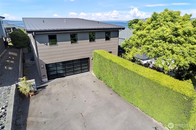 exterior space with a water view, an attached garage, driveway, and metal roof