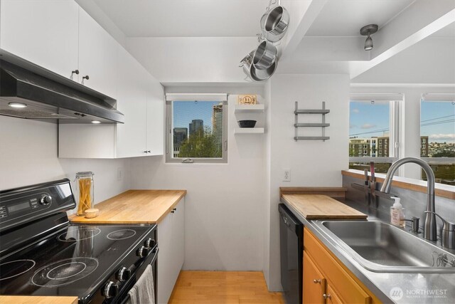 kitchen with black appliances, under cabinet range hood, a sink, light wood-type flooring, and white cabinets
