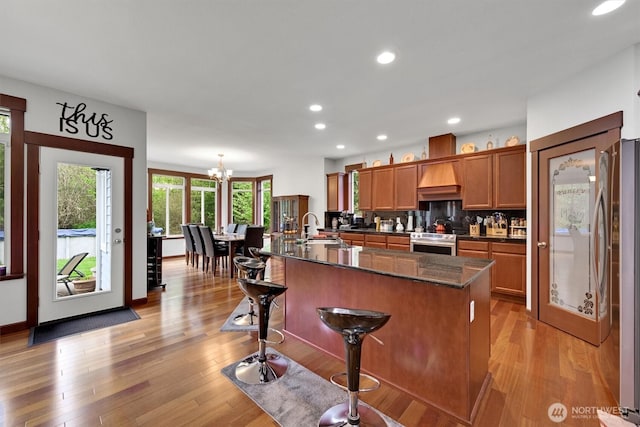 kitchen featuring brown cabinetry, a center island with sink, a chandelier, a sink, and stainless steel appliances