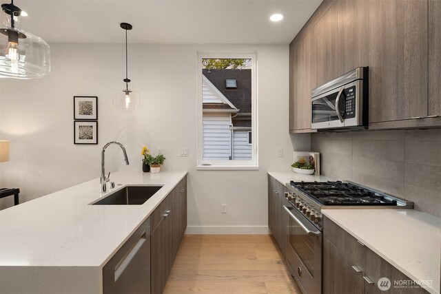 kitchen featuring a peninsula, baseboards, light countertops, a sink, and appliances with stainless steel finishes