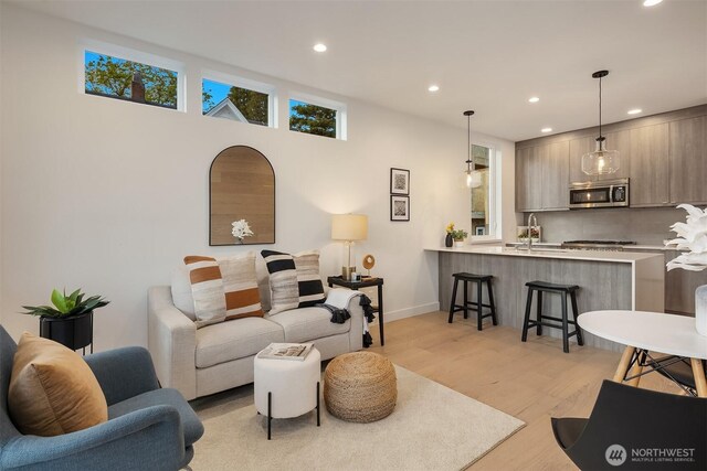 living area with baseboards, light wood finished floors, and recessed lighting