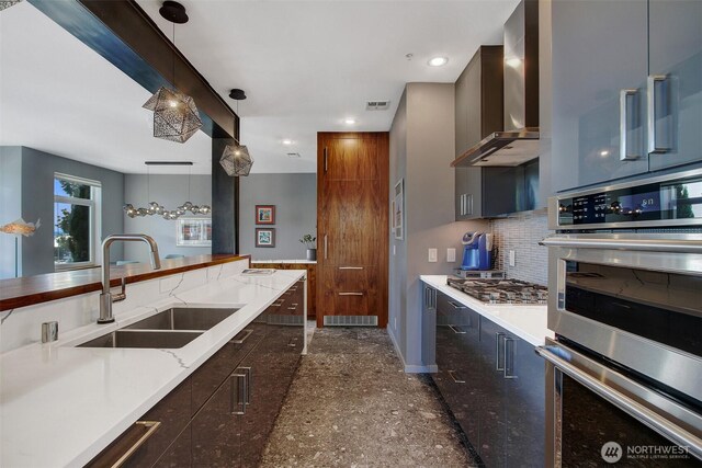kitchen featuring wall chimney range hood, visible vents, a sink, baseboards, and stainless steel appliances