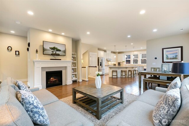 living room featuring recessed lighting, a warm lit fireplace, and wood finished floors