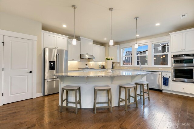 kitchen with white cabinets, light stone countertops, stainless steel appliances, tasteful backsplash, and under cabinet range hood