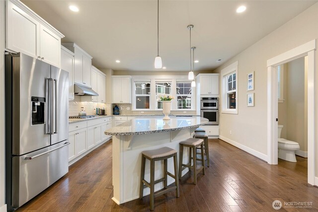 kitchen featuring white cabinets, a center island, stainless steel appliances, baseboards, and tasteful backsplash