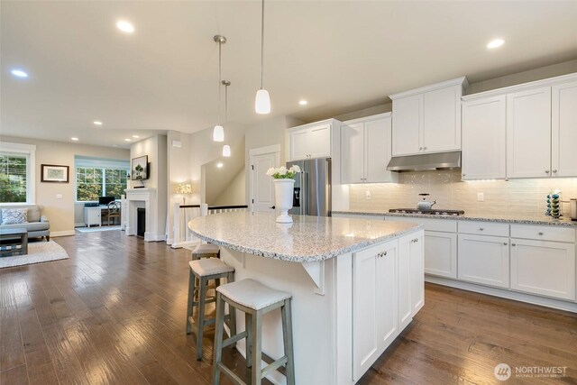 kitchen with a kitchen island, under cabinet range hood, white cabinets, tasteful backsplash, and appliances with stainless steel finishes