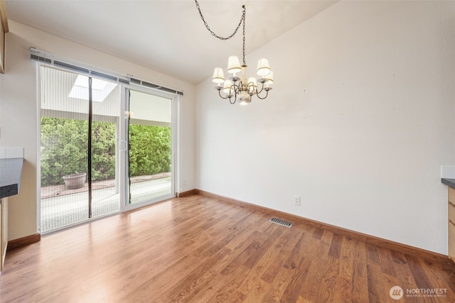 unfurnished dining area featuring visible vents, baseboards, wood finished floors, and a chandelier