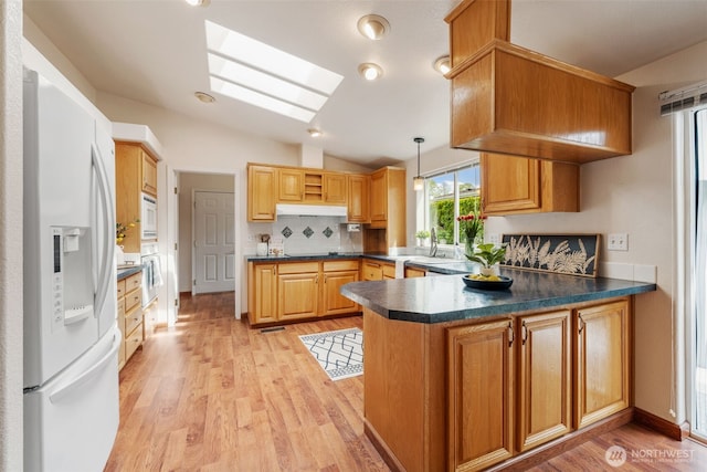 kitchen featuring vaulted ceiling with skylight, decorative backsplash, a peninsula, light wood finished floors, and white appliances