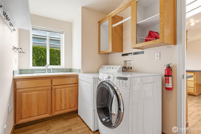 washroom with a sink, separate washer and dryer, light wood-type flooring, and cabinet space