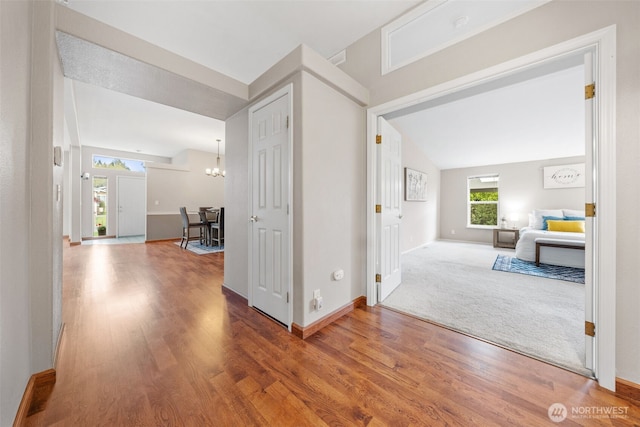 hallway featuring baseboards, a notable chandelier, and wood finished floors