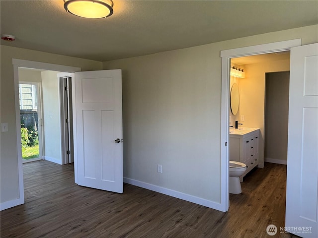 unfurnished bedroom featuring dark wood finished floors, baseboards, and ensuite bathroom