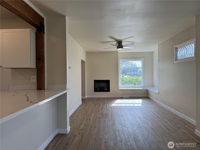 unfurnished living room with wood finished floors, a ceiling fan, a fireplace, and baseboards