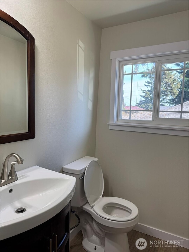 half bath with healthy amount of natural light, toilet, vanity, and wood finished floors