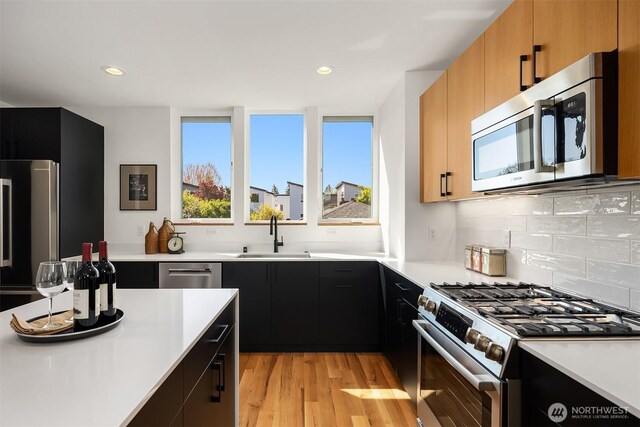 kitchen with appliances with stainless steel finishes, a sink, light countertops, dark cabinets, and light wood-style flooring