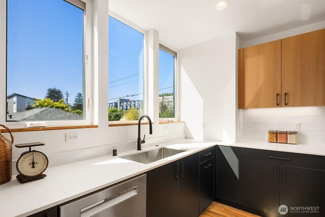 kitchen with dark cabinetry, a sink, dishwasher, and light countertops