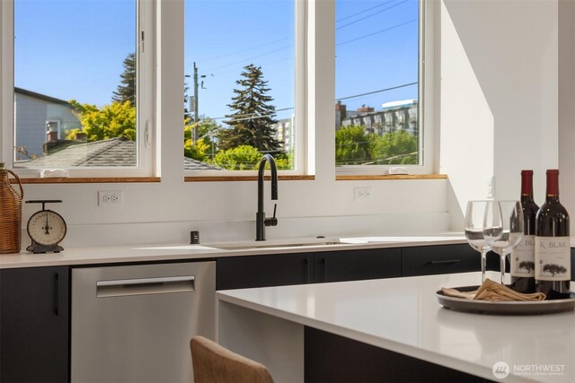kitchen with dark cabinetry, a sink, dishwasher, and light countertops