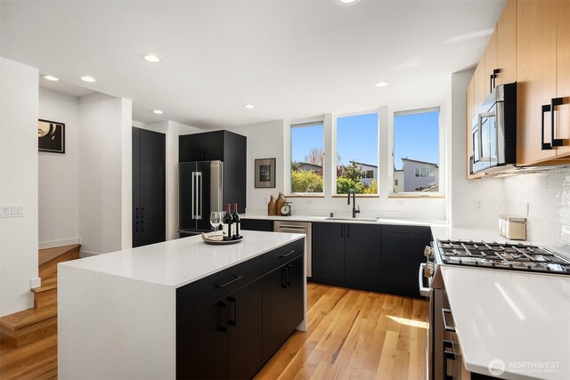kitchen with dark cabinetry, stainless steel appliances, a sink, and light wood-style flooring