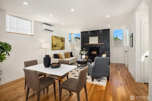 dining area with a premium fireplace, baseboards, a wall unit AC, and light wood-type flooring