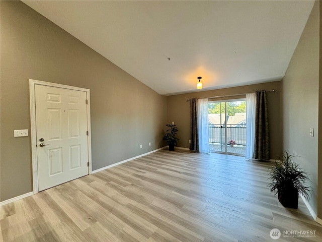 spare room featuring baseboards, lofted ceiling, and light wood-type flooring