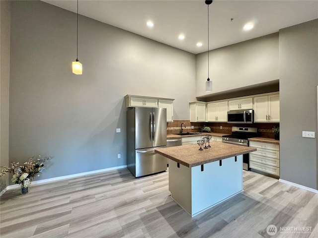 kitchen featuring baseboards, a high ceiling, light wood-type flooring, a sink, and stainless steel appliances
