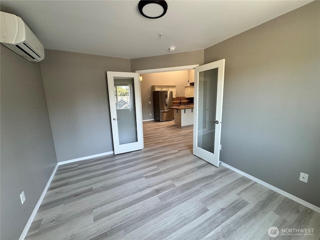 unfurnished room featuring french doors, baseboards, a wall mounted AC, and light wood-type flooring