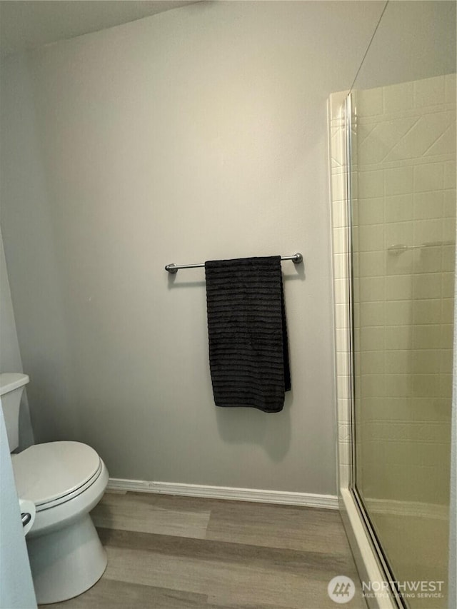 full bath featuring toilet, baseboards, tiled shower, and wood finished floors
