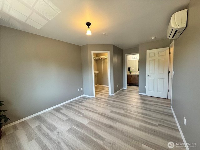 unfurnished bedroom featuring light wood-style floors, baseboards, a wall mounted AC, and a spacious closet