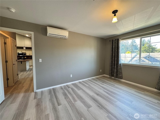 unfurnished room featuring baseboards, a wall unit AC, and light wood-style flooring