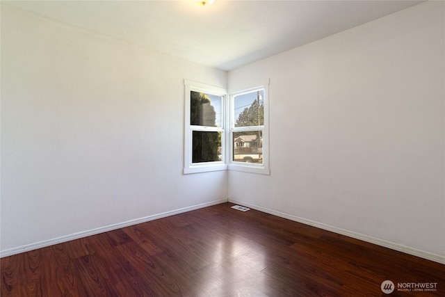 spare room featuring baseboards, dark wood-style floors, and visible vents