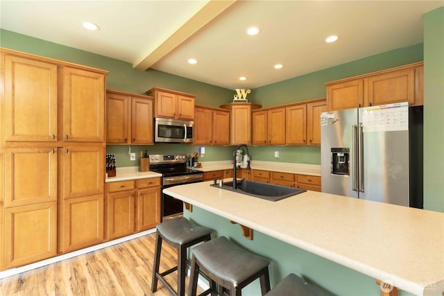 kitchen with appliances with stainless steel finishes, a sink, a breakfast bar area, recessed lighting, and light wood-style flooring