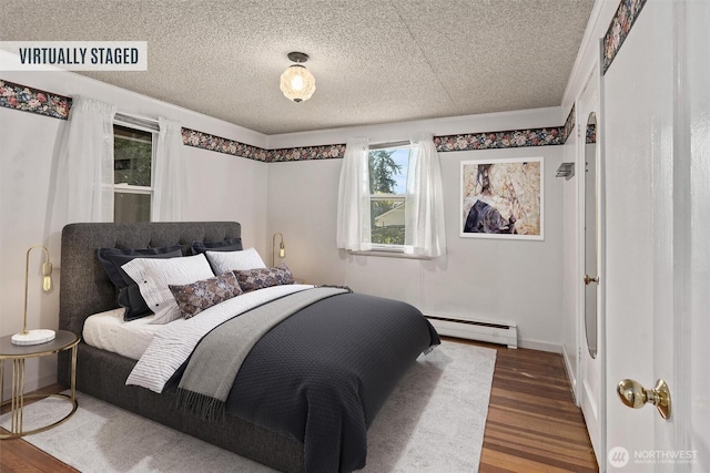 bedroom with a baseboard heating unit, wood finished floors, multiple windows, and a textured ceiling