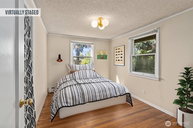 bedroom with crown molding, a textured ceiling, wood finished floors, baseboard heating, and baseboards
