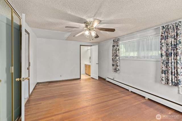 unfurnished bedroom featuring baseboard heating, wood finished floors, a textured ceiling, a ceiling fan, and connected bathroom