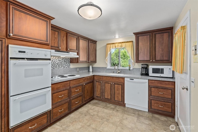 kitchen with white appliances, under cabinet range hood, a sink, light countertops, and decorative backsplash