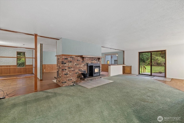 unfurnished living room with carpet flooring, a wood stove, a textured ceiling, wood walls, and a wainscoted wall