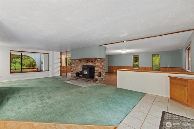 unfurnished living room with light carpet, a wood stove, a textured ceiling, wood walls, and a wainscoted wall