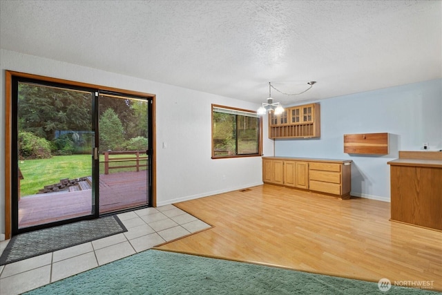 unfurnished dining area with a textured ceiling, a notable chandelier, baseboards, and light wood-type flooring