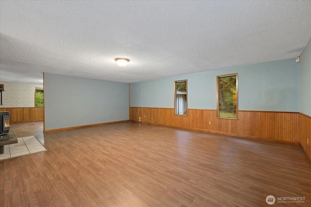 interior space with a wood stove, wainscoting, a textured ceiling, and wood finished floors