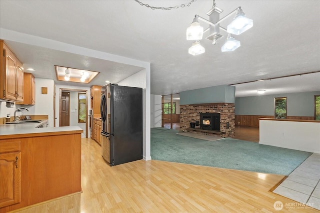kitchen featuring brown cabinetry, freestanding refrigerator, light wood-style floors, light countertops, and a sink