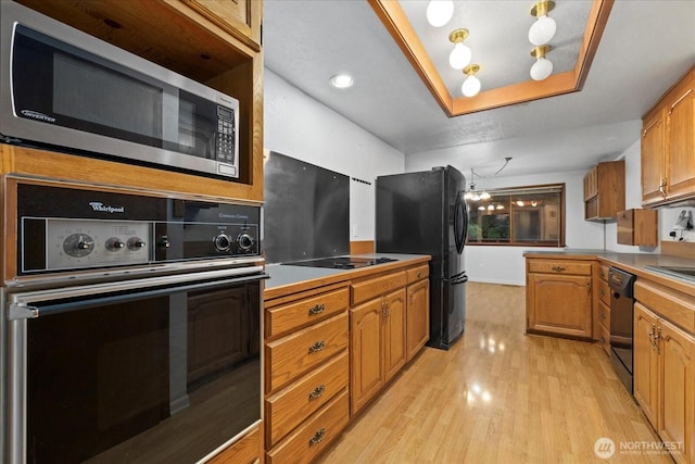 kitchen featuring a raised ceiling, brown cabinetry, light wood finished floors, and black appliances
